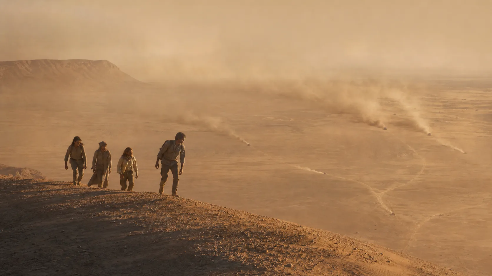 A desert guide leads three women over a high ridge while distant pursuers converge through a sandstorm.